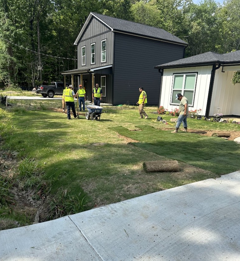 Landscaping crew in hi-vis vests laying fresh green sod across a residential yard in front of new homes